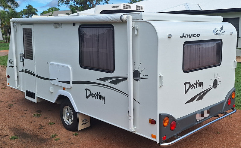 White Jayco Destiny travel trailer parked on a dirt surface with trees and buildings in the background.