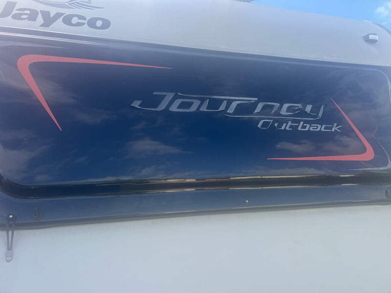 Journey Outback logo on a vehicle window with a cloudy sky reflection.